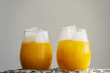 Orange juice or cocktail with ice in glass, cold summer lemonade on light gray background