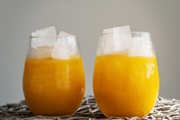 Orange juice or cocktail with ice in glass, cold summer lemonade on light gray background