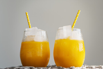 Orange juice or cocktail with ice in glass, cold summer lemonade on light gray background
