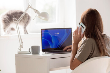 A young, happy, beautiful freelance business woman sitting in a home office with a laptop and a smartphone in her hands. A woman works at home or makes purchases in an online store.