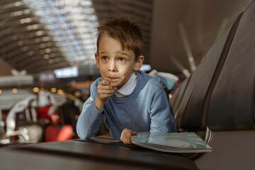 Little boy holding a book in the waiting room at the airport before the flight and looking away