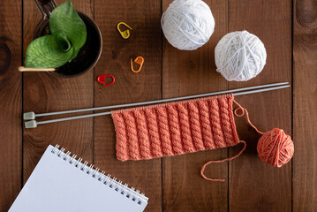 Knitting on spokes with a pattern. Flat lay with yarn, knitting needles, notepad on a wooden table. Hobby concept.
