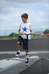 Fototapeta premium Active ten year old boy riding a scooter in the summer skate park