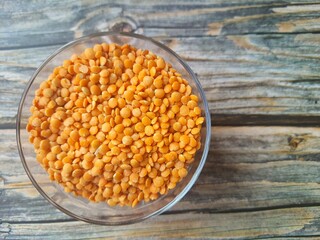 Orange lentils in a bowl on wooden table, top view. Culinary lens.
