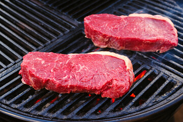 Raw dry aged wagyu roast beef steak grilled as close-up on a charcoal grill with fire and smoke