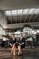 Obraz na płótnie Canvas Two flight attendants sitting on the seats in the airport terminal
