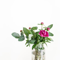 Blooming bouquet of pink peony flowers and green eucalyptus branches in glass vase on white isolated background. Feminine minimalist greeting card mock up template with copy space.