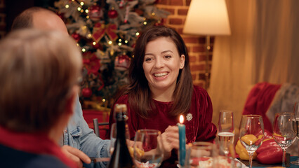 Beautiful wife chatting with senior woman while enjoying Christmas dinner at home. Festive family members eating traditional home cooked food while celebrating winter holiday. Tripod shot