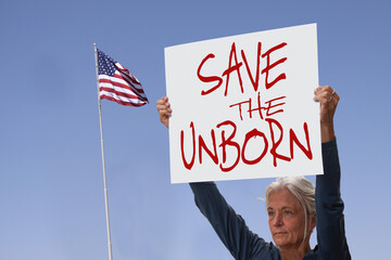 Protester holding sign saying Save the unborn. Woman with placard against abortion rights at...