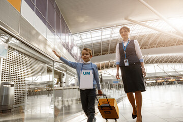 Female airport worker helps a little boy to find correct gate for boarding at the airport