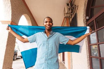 Wide angle portrait of a proud and smiling young man holding a flag of Honduras. - obrazy, fototapety, plakaty