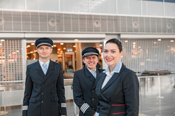 Fototapeta premium Happy two pilots and stewardess standing in the airport terminal