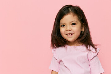 a cute little girl is standing on a pink background in a pink T-shirt, smiling happily and turning her head in different directions and frowning a little. The theme of children's carelessness and fun