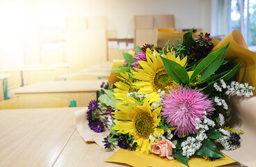 A bouquet of autumn flowers lies on a table in the classroom. Greeting card with the beginning of...