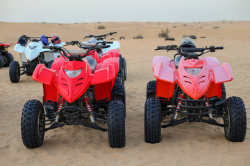 Two red ATVs stand in sand dunes. Orange desert sand landscape
