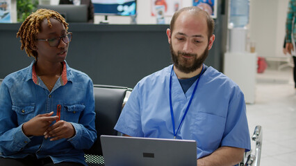 Obraz premium Diverse people analyzing medical diagnosis on laptop in waiting area, woman and male nurse talking about disease and treatment in hospital reception. Specialist consulting patient in clinic lobby.