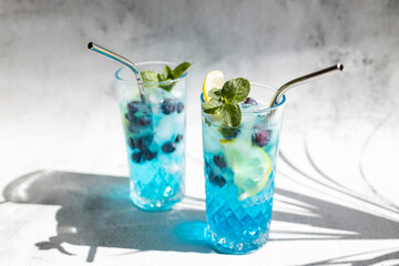 Colorful summer alcoholic blue drink with ice and fresh blueberries, garnished with lemon slices...