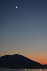 Sunset colors in the sky and reflected on the sea, with the moon and town lights at a distance. Euboea (Evia), Greece