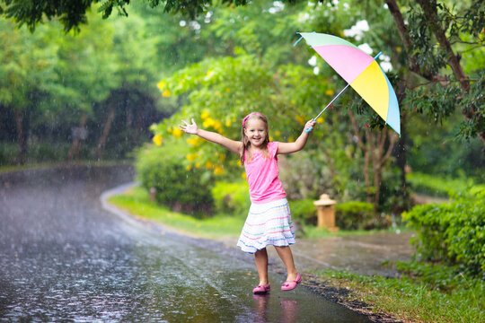 Kid with umbrella playing in summer rain.