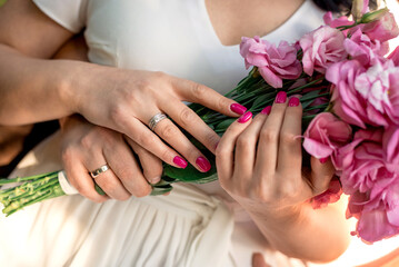 hugging hands of newlyweds with rings and flowers close-up