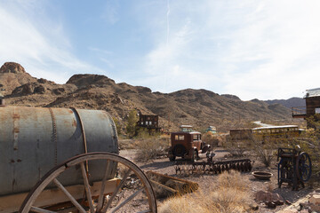 1932 American sedan sits rusting near wagon and vintage school bus under the hot desert sun among...