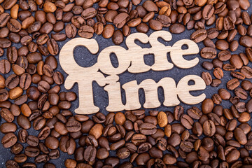 Texture background of coffee beans for design with the inscription coffee time. Coffee grains scattered on the table