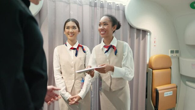 4K Woman flight attendant checking boarding pass and provide service to passenger in airplane. Passenger keep baggage in luggage compartment over the seat. Airline business and travel vacation concept