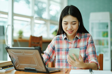 Young asian woman study in front of the laptop computer and and using headphones with phone at...