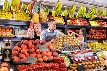 Young man selling a fresh kiwi and other fruits on a supermarket