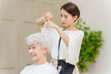 白髪の女性の髪を切る美容師 - obrazy, fototapety, plakaty