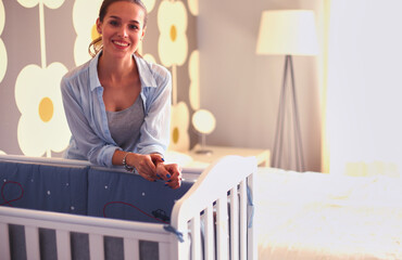 Young woman standing near children's cot. Young mom