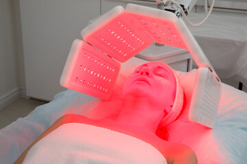 An elderly woman undergoes a facial rejuvenation procedure. Woman face lt Red light treatment At...