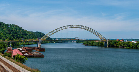 Obraz premium The West End Bridge that spans the Ohio River and connects the north side and the west end in Pittsburgh, Pennsylvania, USA. Several barges and a tugboat are moored to the west end shoreline