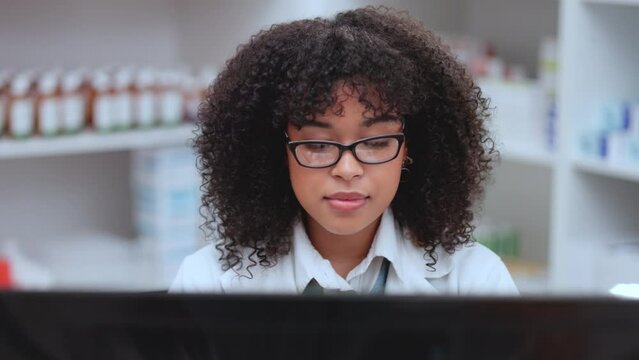 Pharmacist, medical and healthcare professional with computer in pharmacy reading, researching and learning about new medicine. Smiling, happy and friendly afro woman typing in a medication drugstore