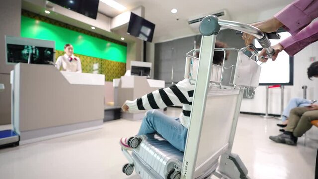 4K African woman with her kid walking to airline ground staff at check in counter and get boarding pass ticket in airport terminal. Airline service business and airplane transportation concept