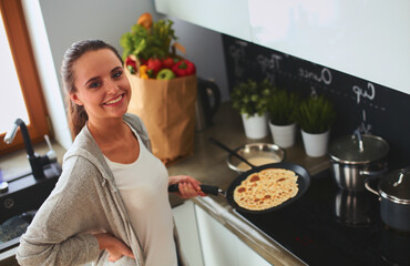 Young woman cooking pancakes at kitchen standing near stove - 521113233