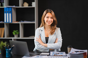 Happy young asian businesswoman sitting on her workplace in the office. Young woman working at laptop in the office
