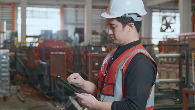 Worker man looking up check list details on a tablet, mechanic is repairing the machine maintenance at metal sheet factory, engineer standing and checking process in industry manufacturing