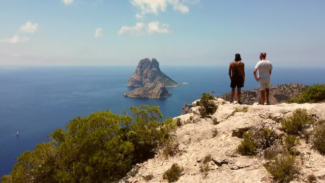 Two hikers enjoy the view of the mysterious island.
Dramatic aerial view flight Very close passing flight drone footage
of cliff edges hike Es Vedra Ibiza summer 2022. 4k from above by Philipp Marnitz