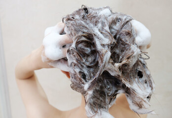 Woman shampooing her hair with both hands on her head in front of a white background.
