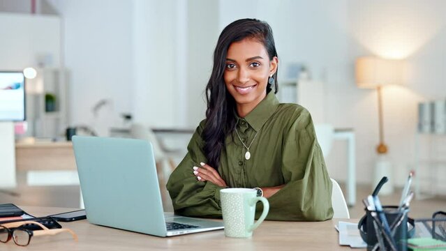 Proud, happy and confident business woman typing on a laptop and looking at the camera in her office. Portrait of a young female entrepreneur writing a project smiling in her workplace