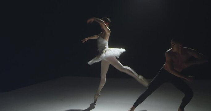 Romantic young ballet couple dance on dark stage with backlight.