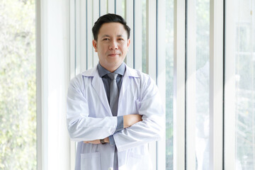 Portrait of asian senior doctor standing and cross arms posing in  lobby hospital.