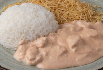 Focus on chicken stroganoff (estrogonofe de frango) with rice and stick potato on green plate.