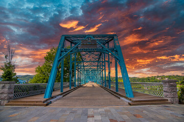a stunning shot of the Walnut Street Bridge surrounded by lush green trees with powerful clouds at sunset in Chattanooga Tennessee USA
