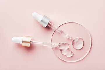 Two pipettes with different samples of gels cosmetic products in petri dish on pink background