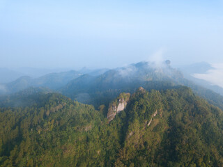 A panoramic view of the foggy Mountains with dense of forest. Blue sky with clouds over layers of green hills and mountains. Copy space.  Menoreh Hill, Central Java, Indonesia