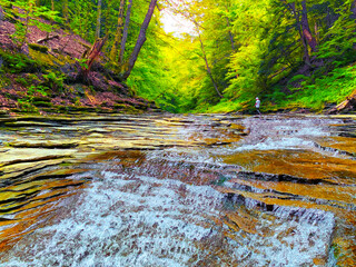 Steam waterfall in the middle of greenery forest splash water peacefully flowing pass rocks and stone over the trees morning color warm sunlight sky background.