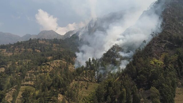 fire in mountain forest. aerial view forest fire and smoke on slopes hills. wild fire in mountains in tropical forest, Java Indonesia. natural disaster fire in Southeast Asia