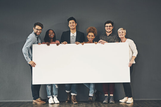 A group of professionals holding a blank board or sign with copy space on a grey background. Diverse team advertising space or a vacancy at their startup. Smiling colleagues advertising on a placard
